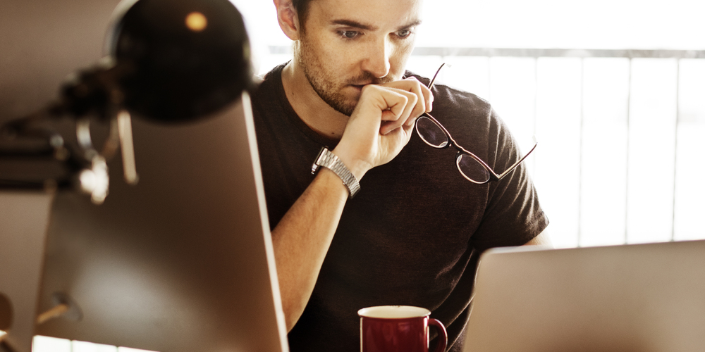 Guy looking at laptop holding his glasses